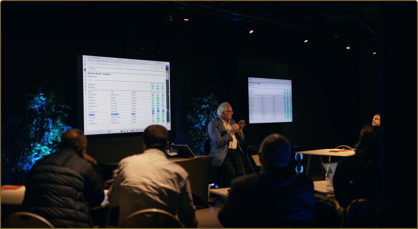 A senior trainer presenting team results on screen during an Elite Teams debrief